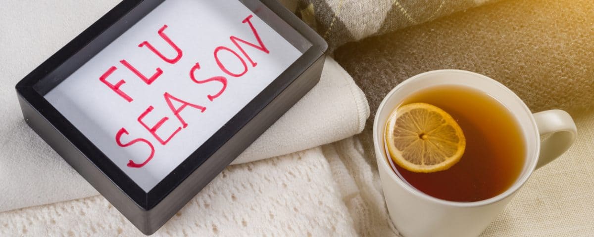 Flu season text in frame. Background warm woolen clothes, cup of hot tea