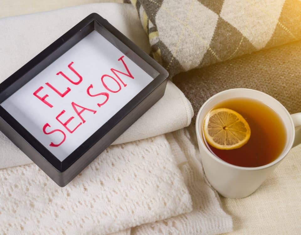 Flu season text in frame. Background warm woolen clothes, cup of hot tea